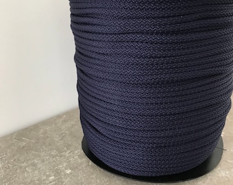 May include: A spool of navy blue rope. The rope is tightly wound and has a textured surface. The spool is black and sits on a gray surface. The rope appears to be made of a durable, synthetic material.