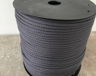 May include: A large spool of dark gray cord featuring a tightly woven, braided texture. The cord is wound neatly around a black plastic cylindrical reel with a circular top and bottom, creating a uniform and dense stack of gray material.
