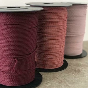 Puede incluir: Tres carretes de cordón en tonos rojos y rosas. Los carretes cilíndricos tienen el cordón cuidadosamente enrollado. Los colores varían desde un borgoña intenso hasta un rosa rubor suave, ideal para proyectos de manualidades.