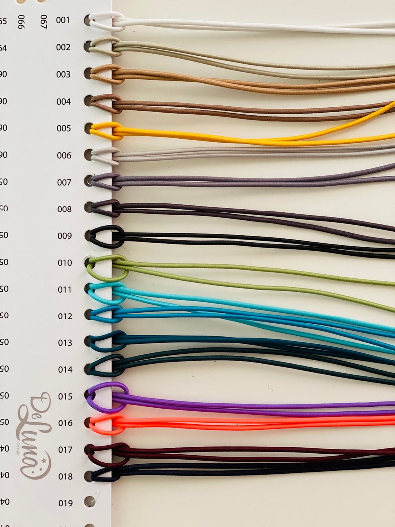 May include: A colour chart showing a selection of elastic cords. The cords are in a variety of colours, such as white, beige, brown, yellow, grey, black, teal, blue, purple, orange, and burgundy. Each cord is looped at the top.