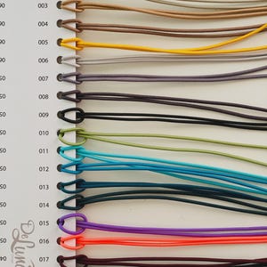 May include: A color chart featuring a variety of cords in different colors, including white, tan, brown, yellow, purple, orange, and black. Each cord is attached to a numbered tag. The cords are likely used for crafting or jewelry making.
