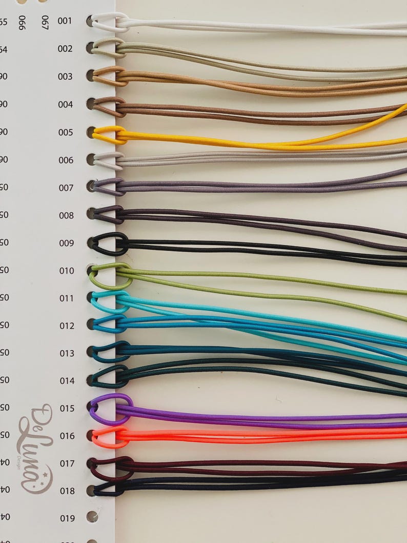 May include: A color chart featuring a variety of cords in different colors, including white, tan, brown, yellow, purple, orange, and black. Each cord is attached to a numbered tag. The cords are likely used for crafting or jewelry making.