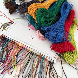May include: A collection of colorful elastic cords in various hues, including green, yellow, blue, and red. A color chart displays numerous cord samples with the text "nusinerk" and "REFLECTIVE". Bundles of cords are neatly arranged, showcasing a range of crafting supplies.
