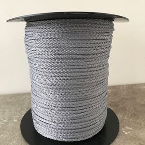 May include: A spool of gray braided cord wrapped around a black plastic base.