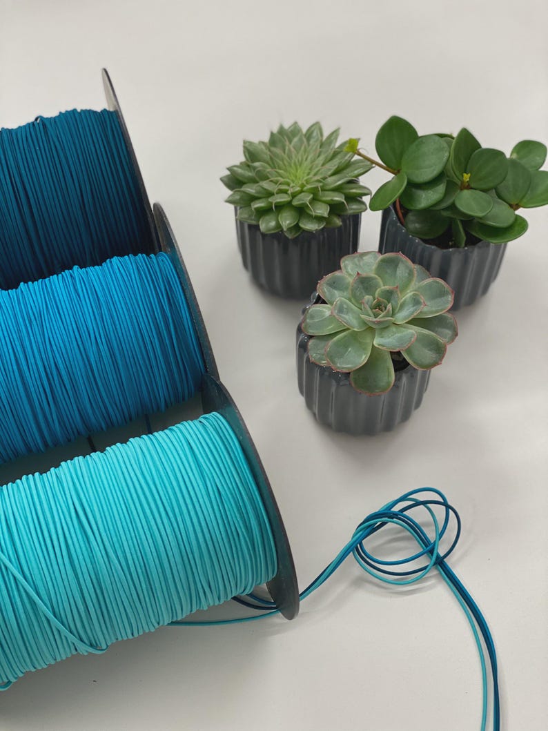 Puede incluir: Tres carretes de cord&oacute;n verde azulado, turquesa y aguamarina se encuentran junto a tres peque&ntilde;as suculentas en macetas. El cord&oacute;n est&aacute; enrollado firmemente en carretes negros. Las suculentas est&aacute;n en macetas grises oscuras y acanaladas.