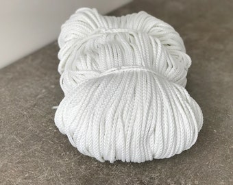 May include: A close-up of a large spool of white cotton rope. The rope is tightly wound and appears to be made of a soft, natural material.