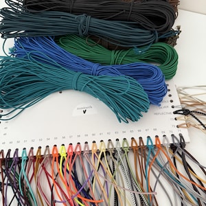 May include: A color sample card labeled nusinerk with a heart icon, featuring multiple bundles of elastic cord in shades of brown, black, green, and blue, with individual numbered strands in various colors hanging from the bottom edge.