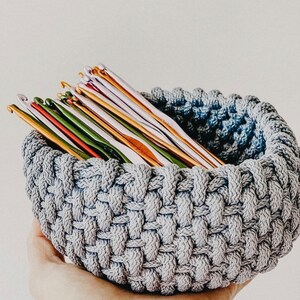 May include: A gray crocheted bowl filled with a variety of colorful crochet hooks.