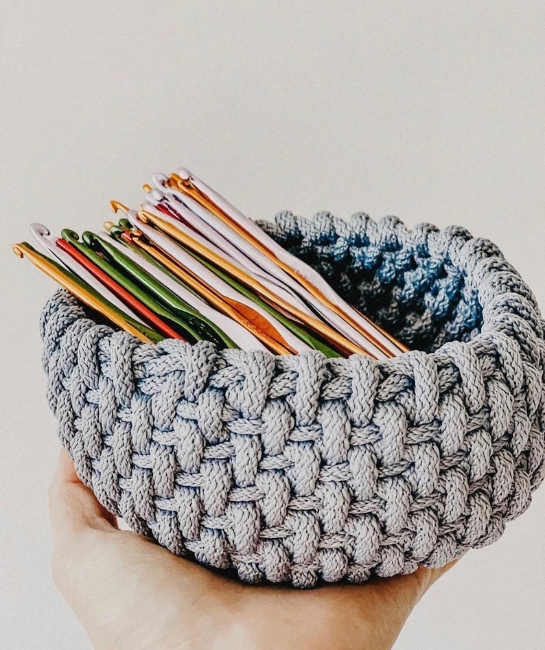 May include: A gray crocheted bowl filled with a variety of colorful crochet hooks.