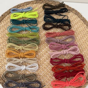 Op de afbeelding: Een verzameling van achtentwintig elastische haarelastiekjes gerangschikt in twee verticale kolommen. De elastiekjes hebben verschillende effen kleuren, waaronder neongeel, blauw, groen, bruin, roze, rood, oranje, wit, beige en grijs, elk in een lus.