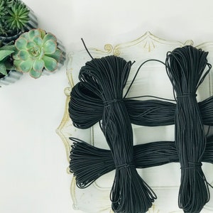 May include: Several bundles of black elastic cord are arranged on a decorative white tray. The cord is tightly wound and tied. Green succulents in small gray pots are in the upper left corner.