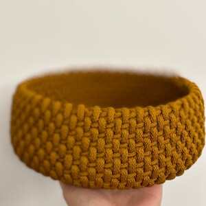 May include: A round, woven basket made of thick, mustard yellow rope. The basket is empty and has a slightly rounded bottom.