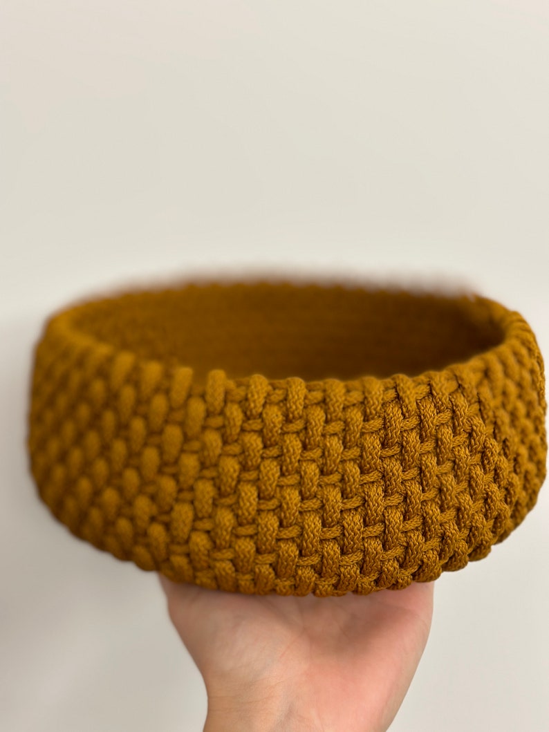 May include: A round, woven basket made of thick, mustard yellow rope. The basket is empty and has a slightly rounded bottom.