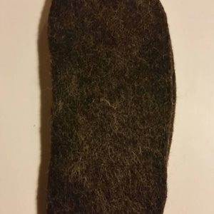 May include: A dark brown felt insole for shoes or slippers. The insole is made of a soft, fuzzy material and has a slightly oval shape.