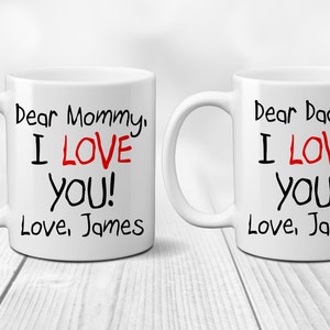 May include: Two white ceramic mugs with black text and red hearts. The text on the mugs reads "Dear Mommy, I LOVE You! Love, James" and "Dear Daddy, I LOVE You! Love, James".