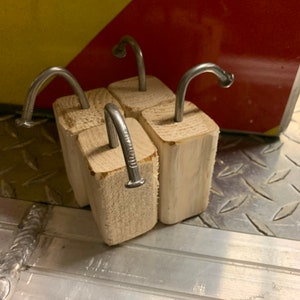 May include: Four wooden blocks with bent nails sticking out of the top. The blocks are arranged in a square shape.