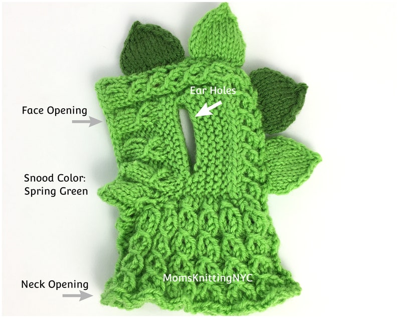 Op de afbeelding: Een lentegroene gebreide snood met een dinosaurusontwerp. De snood heeft een gezichtsopening, oor gaten en een nekopening. Het ontwerp bevat bladvormige accenten en de tekst "MomsKnittingNYC".