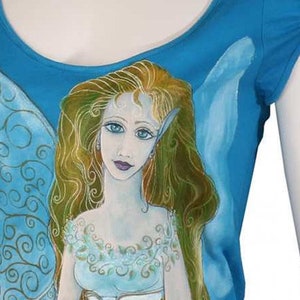 May include: A turquoise blue t-shirt with a hand-painted design of a fairy with blue wings and long blonde hair. The fairy is wearing a white corset and a blue skirt. The t-shirt has a gold signature in the bottom right corner.