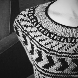 K&ouml;nnte beinhalten: Ein schwarz-wei&szlig;er Strickpullover mit geometrischem Muster. Der Pullover hat einen Rundhalsausschnitt und ist aus einem weichen, warmen Material gefertigt.