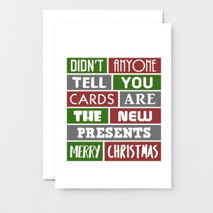 Pu&ograve; includere: Un biglietto d'auguri bianco con una griglia di rettangoli rossi, verdi e grigi. Il testo recita: DIDN'T ANYONE TELL YOU CARDS ARE THE NEW PRESENTS MERRY CHRISTMAS. Il design utilizza un mix di caratteri bianchi con e senza grazie.