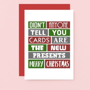 Pu&ograve; includere: Un biglietto d'auguri bianco con una busta rossa che riporta il testo DIDN'T ANYONE TELL YOU CARDS ARE THE NEW PRESENTS MERRY CHRISTMAS in una griglia di blocchi rettangolari verdi, grigi e rossi con caratteri bianchi.