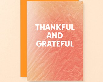 May include: A greeting card with the words "THANKFUL AND GRATEFUL" in white block letters. The card has a textured, gradient background in shades of orange and peach. An orange envelope is behind the card.