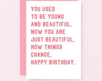 May include: A white greeting card with pink text that reads: YOU USED TO BE YOUNG AND BEAUTIFUL. NOW YOU ARE JUST BEAUTIFUL. HOW THINGS CHANGE. HAPPY BIRTHDAY. The card is partially tucked into a solid pink envelope, creating a layered appearance.