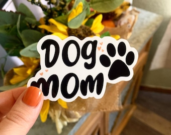 May include: White sticker with black text that reads "Dog Mom" with a black paw print and small pink hearts.