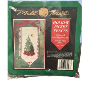 May include: A Mill Hill Holiday Picket Fences cross stitch kit in a green plastic package. The kit features a white fabric band with a green Christmas tree, red poinsettias, and a gold moon. Text includes Holiday Picket Fences, Starlight Trees, MHPF11, and 36W X 59H.