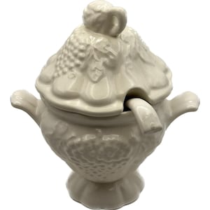 May include: Off-white ceramic soup tureen with a lid and ladle. The tureen has two handles and a pedestal base. The lid is decorated with a grape cluster design. The ladle rests inside the tureen. The tureen is a vintage style.