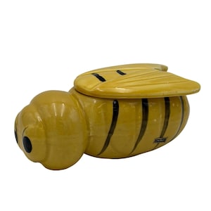 May include: A ceramic bee-shaped trinket box with a yellow body and black stripes. The wings are yellow with black accents. The box has a lid and is marked "JAPAN".