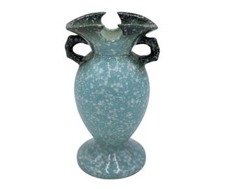May include: A speckled turquoise vase with a flared rim and two handles. The vase has a pedestal base and a speckled white pattern. The rim and handles are dark gray. The vase is a decorative item.