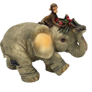 May include: A detailed figurine of an elephant with a monkey riding on its back. The elephant is gray with large ears and a trunk, and the monkey is brown. The elephant's head is adorned with a branch and red berries.