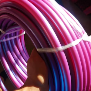 May include: A close-up of a purple and pink hoop, wrapped with white tape. The hoop is made of multiple layers of plastic tubing.