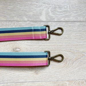 May include: A colorful striped fabric strap with gold metal clasps. The strap is pink, yellow, blue, and black.