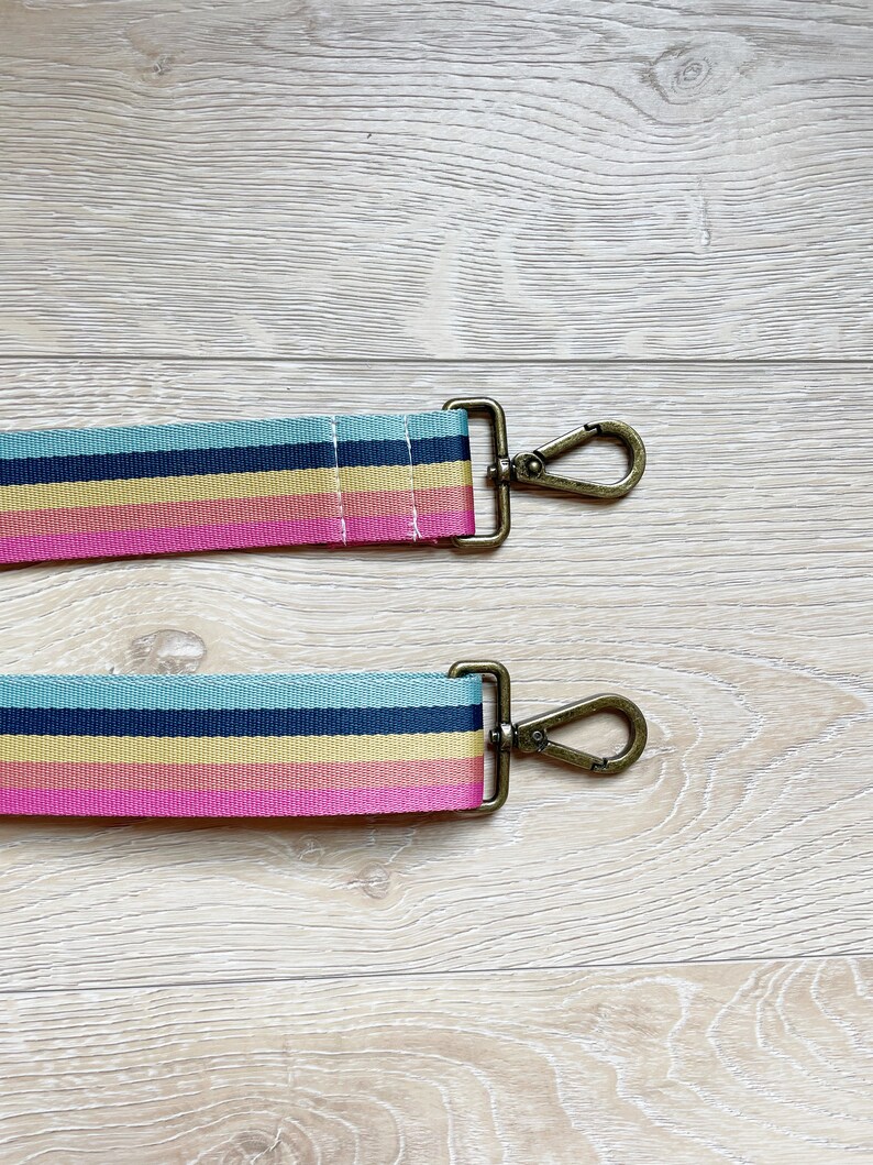 May include: A colorful striped fabric strap with gold metal clasps. The strap is pink, yellow, blue, and black.