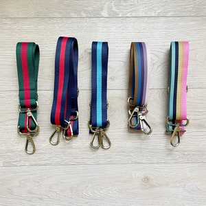 May include: Five colorful striped straps with gold clasps. The straps are made of woven fabric and have a variety of colors, including red, blue, green, pink, and yellow.