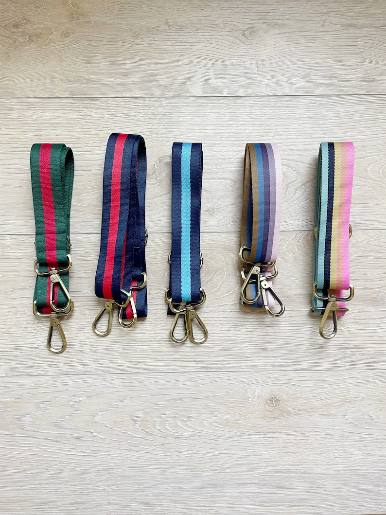May include: Five colorful striped straps with gold clasps. The straps are made of woven fabric and have a variety of colors, including red, blue, green, pink, and yellow.