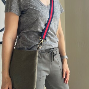 May include: A gray t-shirt with a red and blue striped shoulder strap and a green canvas tote bag.