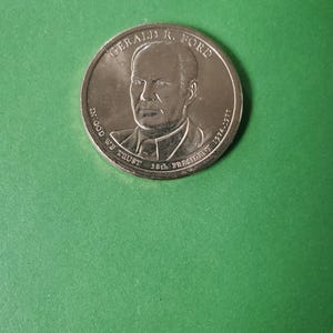 May include: Silver-colored coin with a portrait of Gerald R. Ford, the 38th President of the United States, and the text "GERALD R. FORD 38th PRESIDENT 1974-1977" around the edge. The coin also has the text "IN GOD WE TRUST" on the left side.