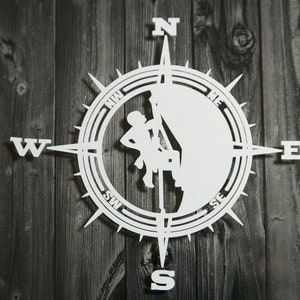 Peut inclure: Boussole blanche avec une silhouette d'une personne escaladant une falaise. La boussole indique le nord, le sud, l'est et l'ouest.