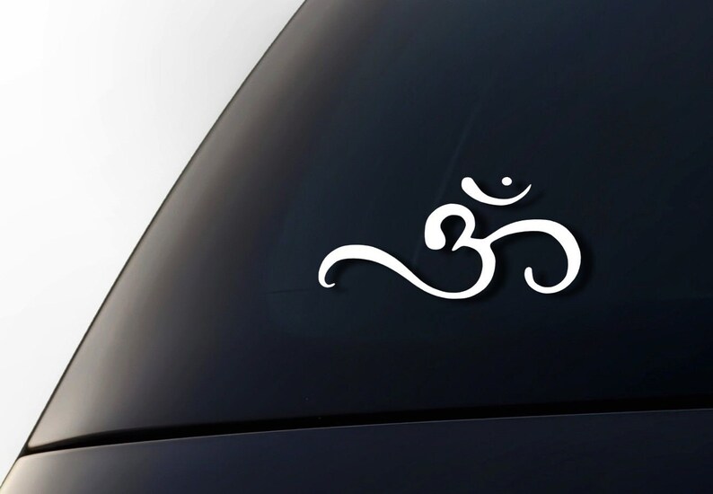 Peut inclure: Autocollant en vinyle blanc du symbole Om, un son sacr&eacute; et un symbole spirituel dans l'hindouisme, le bouddhisme et le ja&iuml;nisme. L'autocollant est sur une vitre de voiture noire.