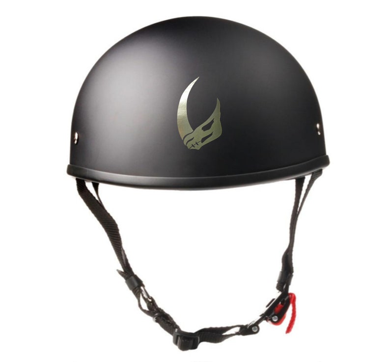 Puede incluir: Un casco de moto negro con un dise&ntilde;o de calavera y cuerno plateado. El casco tiene una correa de barbilla con una hebilla roja.
