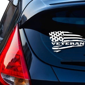 May include: A white vinyl decal with a distressed American flag and the word "Veteran" on a black car.