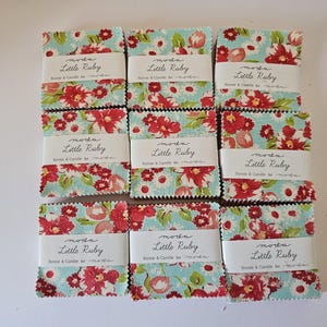 May include: Nine stacks of square fabric swatches featuring a light blue background with red and white floral patterns. Each stack is secured with a white paper band printed with the text moda Little Ruby Bonnie & Camille for moda.