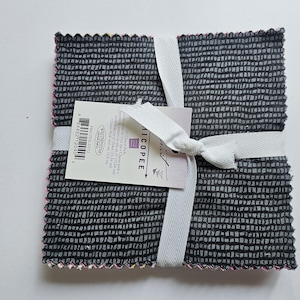 May include: A square stack of fabric squares tied with a white ribbon. The top fabric features a dark gray grid pattern. A paper tag is attached, labeled Chicopee 5 inch Charm Pack, indicating the squares measure 5 inches by 5 inches.