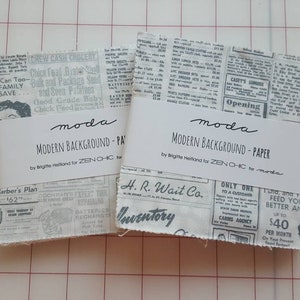 May include: Two stacks of fabric squares featuring a black and white vintage newspaper print. Each stack is secured with a white paper band labeled "moda MODERN BACKGROUND - PAPER by Brigitte Heitland for ZEN CHIC for moda" in black text.