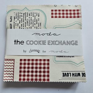 May include: A stack of square fabric pieces with pinked edges, featuring a cream background with red gingham patterns, teal outlines, and black text including the words moda, the COOKIE EXCHANGE, and a recipe for Jam Bars.