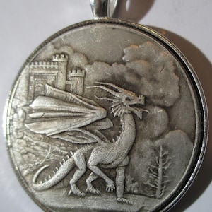 Puede incluir: Pendiente de plata con un diseño de dragón detallado con las alas extendidas, de pie frente a un castillo y un cielo nublado.