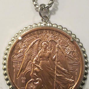 May include: A round copper-toned pendant featuring a relief of an angel holding a staff and scroll, with an eagle at the base. The text URIEL ARCHANGEL is inscribed at the top. The pendant is set in a silver-toned beaded frame on a silver chain.